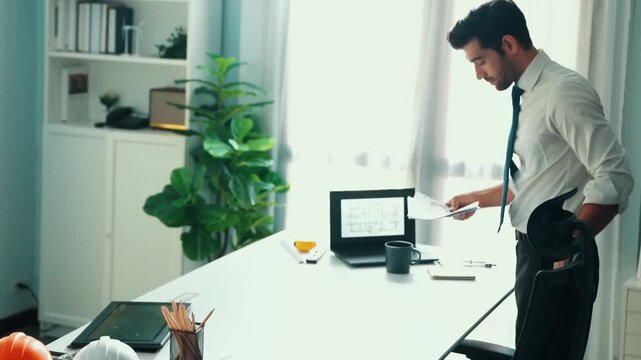 Architect engineer using laptop planning house design at office while sitting at meeting table with blueprint and equipment scatter around.Skilled civil engineer working at blueprint. Alimentation.