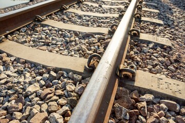 Close-up of a railway track with steel rail, concrete sleepers, and gravel ballast, symbolizing transportation infrastructure, industry, travel, and logistics.