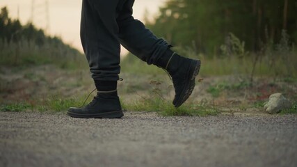 wide shot caucasian trekker boots steady stride gravel, evening road with soft dust kicks, measured movement and calm rhythm, cinematic framing, country roadside atmosphere and enduring pace