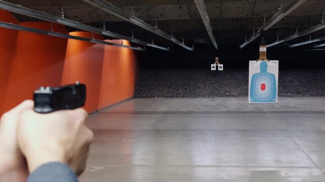 POV person shooting a handgun at paper target inside an indoor shooting range. Firearm training, marksmanship practice, and controlled target shooting in a safe environment.