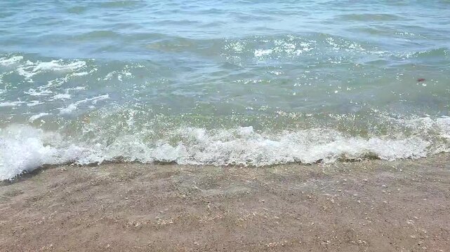 Sea waves with turquoise transparent water rolling onto sand of sandy beach on sunny summer day. Quiet, calm, windless sea. Low angle. From below. Nobody. Nature backdrop. Natural background
