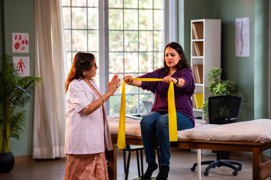 Young woman strengthening shoulders and arms with senior physiotherapist in modern clinic