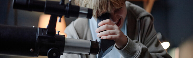 Website header shot of Caucasian child boy examining telescope, demonstrating intense focus and curiosity, engaging in scientific exploration, representing young prodigy keen on astronomy or science © Seventyfour