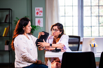 Senior woman doctor measuring blood pressure of young female patient in modern clinic