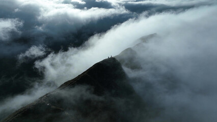 Obraz premium A mountain ridge in thick fog with hikers at the peak, creating a mysterious scene for adventure stories.