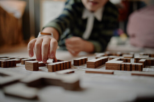 Caucasian child building architectural model with wooden blocks, demonstrating advanced spatial skills and concentration, hand carefully arranging pieces on tabletop, face partially visible