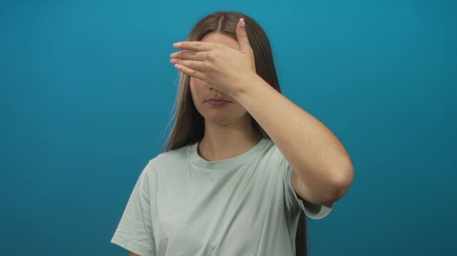 Teenage girl with long brown hair wearing a light green shirt covers her eyes with her hand in a studio environment; vulnerability.