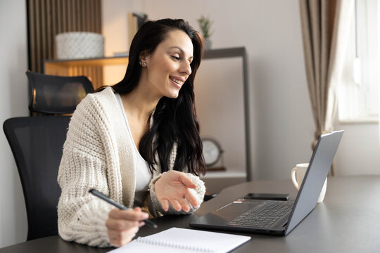 A cheerful woman participates in a virtual meeting while showcasing her well-designed workspace. - Powered by Adobe