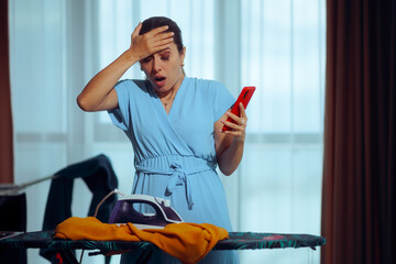 Woman Checking her Phone Forgetting the Iron Burning a Garment. Distracted housewife forgetting she was ironing overusing her smartphone