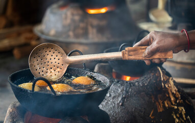 An Assamese woman prepares traditional sweets by deep-frying batter in hot oil over a wood-fired stove, as part of Magh Bihu preparations in Assam, India