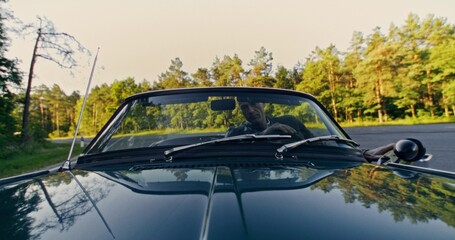 Front view of a man as he gets into a retro convertible, puts on sunglasses and starts driving