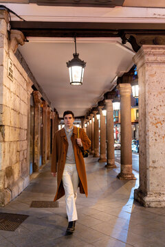 Young man walking city colonnade at night after work
