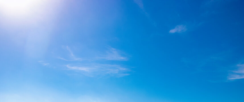 Clear blue sky with wispy clouds and bright sunlight in upper corner, gradient sky tones and natural cloud texture for weather background, daylight atmosphere and outdoor nature environment visuals.