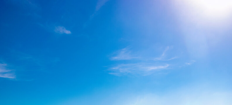 Clear blue sky with wispy clouds and bright sunlight in upper corner, gradient sky tones and natural cloud texture for weather background, daylight atmosphere and outdoor nature environment visuals.