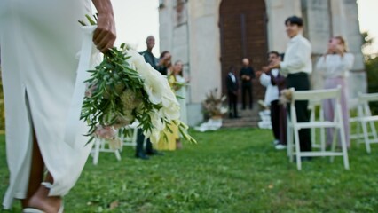The bride walks past the guests to the groom waiting for her near the church, close-up of the bouquet in her hands © m-art