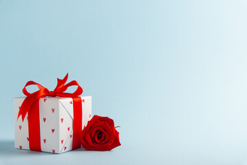 Gift, present box decorated with red ribbon bow and hearts, red rose flowers on light blue background. Valentine's day, 14 February, birthday, 8 march women's day gift. Love and romance.