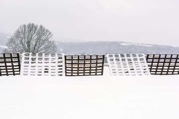 Snow-Covered Metal Snow Fences in Winter Landscape. Winter landscape with snow-covered metal snow fences stretching across a frozen field, close to the village.