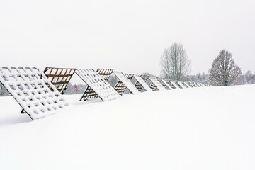 Snow-Covered Metal Snow Fences in Winter Landscape. Winter landscape with snow-covered metal snow fences stretching across a frozen field, close to the village.