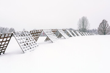 A winter landscape with snow-covered windbreak fence for snow stretching across a frozen field near the village, with a traffic sign visible in the background.