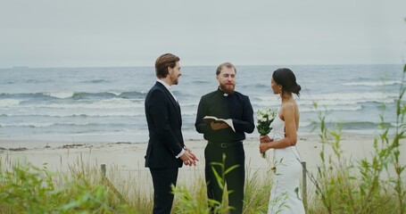 The wedding of a young couple on the seashore, the priest says a speech