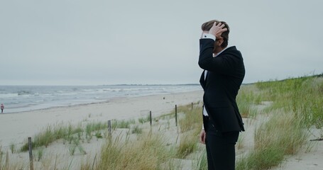 The groom stands on the seashore and looks into the sea