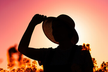 Back lit silhouette of a female farmer standing in blooming cultivated rapeseed crop plantation field