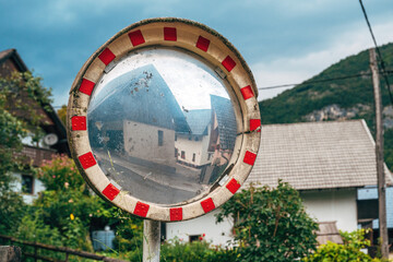 Old convex traffic mirror reflecting a distorted image of village houses, symbolizing perception and reality.