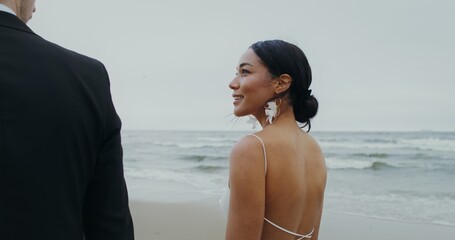 The bride and groom smile and kiss while walking on the beach