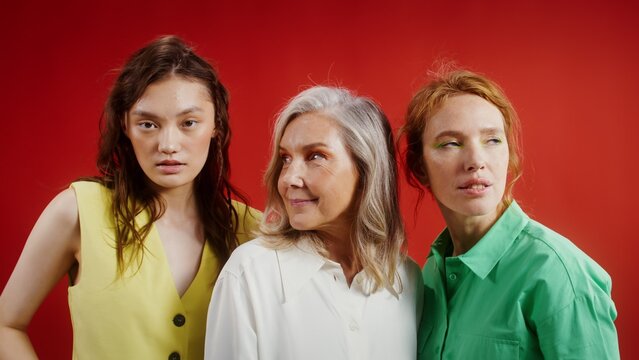 Three women of different ages and nationalities posing against a monochrome background in the studio