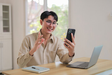 Smiling young man video calling with smartphone from home, engaging in distant communication and virtual meeting