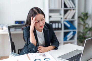 Young Asian businesswoman feeling stressed and frustrated, rubbing her temples due to headache and fatigue from overwork at the office desk