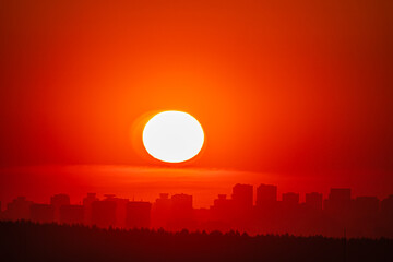A vibrant sunset casts a golden glow over a city, silhouetting its tall buildings