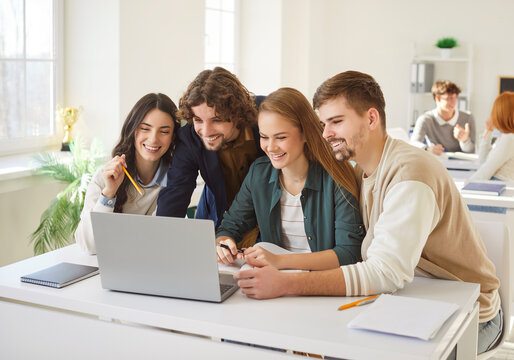 Happy university students or classmates collaborating on task, using laptop in modern classroom. Smiling young people discussing ideas, analyzing data and preparing group project or presentation.