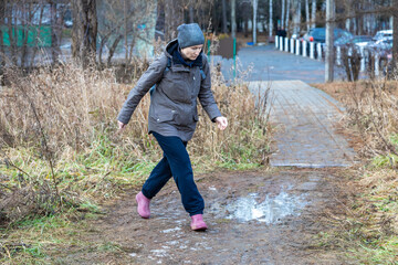 Fototapeta premium Caucasian woman walking on muddy path in rural area, wearing warm coat and hat. Adventure travel and outdoor activity concept for autumn hike.