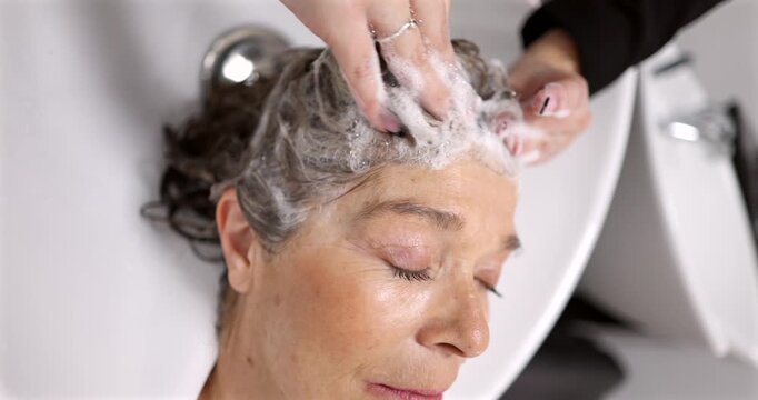 Mature woman with her eyes closed enjoying a relaxing head massage from a hairdresser while getting her hair washed with shampoo and foam in a professional sink at a beauty salon