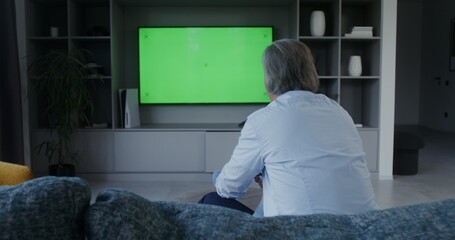 Man playing video game with joysticks sitting in front of green screen TV