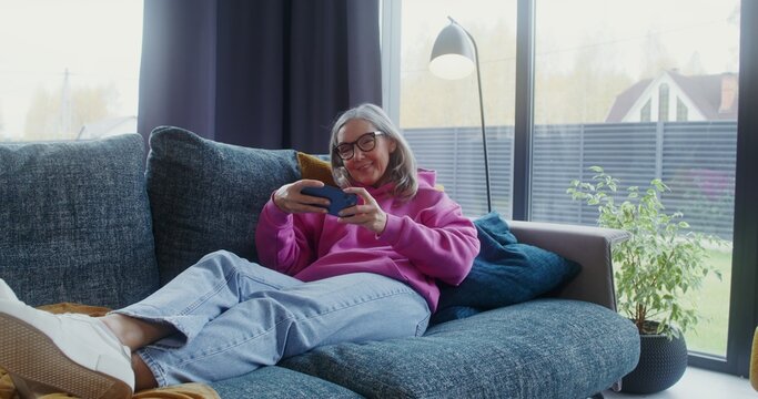 Elderly woman playing mobile phone lying on the sofa at home