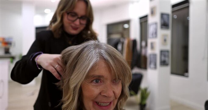 Happy senior woman getting her hair styled by a professional hairstylist at a beauty salon. A female hairdresser is finishing the haircut for an older client, creating volume and shape