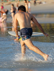 A man in a blue swim trunks is running in the water with a surfboard