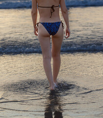 A woman is walking on the beach in a bikini