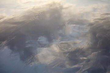Reflection of clouds on sandy water. The clouds are white and scattered. The water is calm and still
