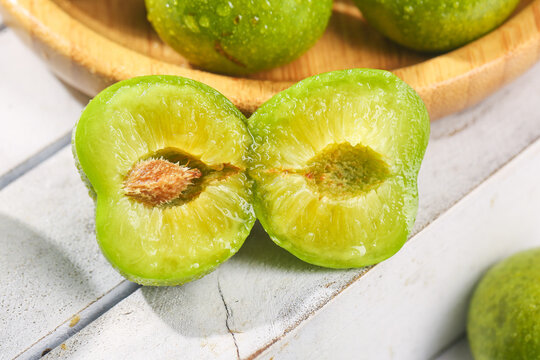 Fresh Green Sichuan Plums with Pit on White Wood Surface