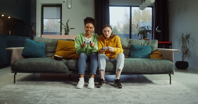 Two female friends playing video games with joysticks at home - Powered by Adobe