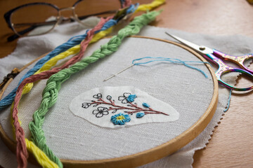 Hand embroidery of blue forget-me-not flower at an embroiderer&rsquo;s workspace. Cozy DIY scene showing handmade craft, slow living lifestyle, creativity and traditional needlework process.