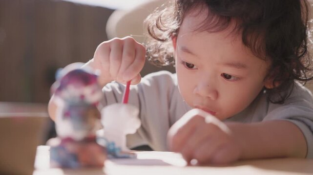 Child carefully coloring a plaster sculpture with a paintbrush, enjoying a creative DIY craft project that develops imagination, focus, artistic expression, fine motor skills, and creativity.
