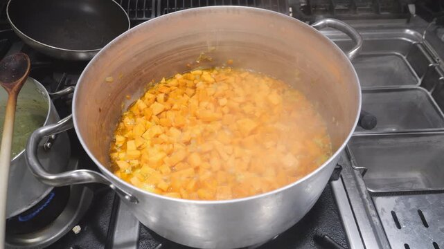 Close view of concass&eacute; cut yams slowly simmering in a metal pot on a kitchen stove, releasing steam during the cooking process for a traditional velout&eacute;, highlighting commercial cuisine
