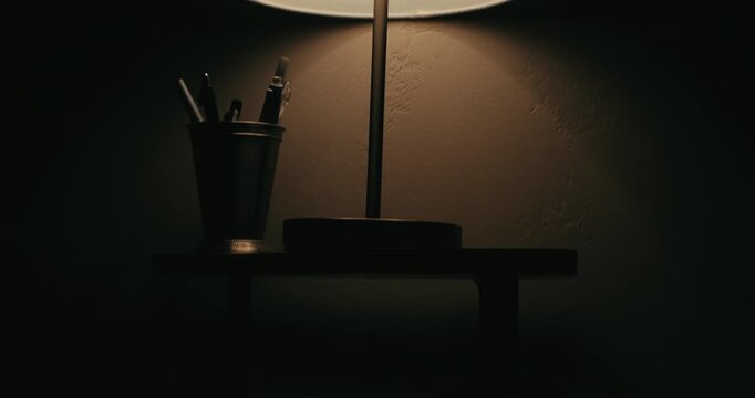 Tilt up toward eerie flickering lamp casting shadows in dark room, pens in cup