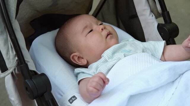 Little asian baby boy is lying outdoor in a stroller. 