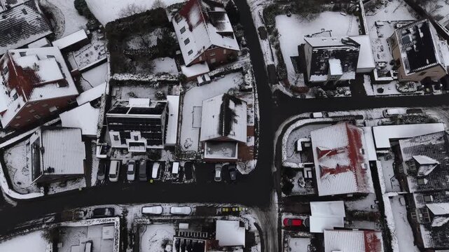 Snow-covered American residential area, showing compact houses, icy roads, parked cars and winter rooftops in quiet suburban neighborhood. Aerial flyover following road shot.