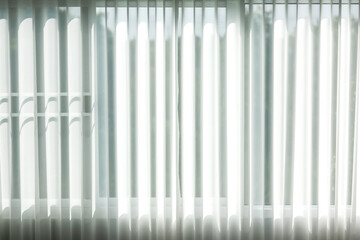 Soft daylight passes through white vertical blinds, creating bright lines, gentle shadows, and a clean minimalist interior mood, ideal for modern home or office background concepts.